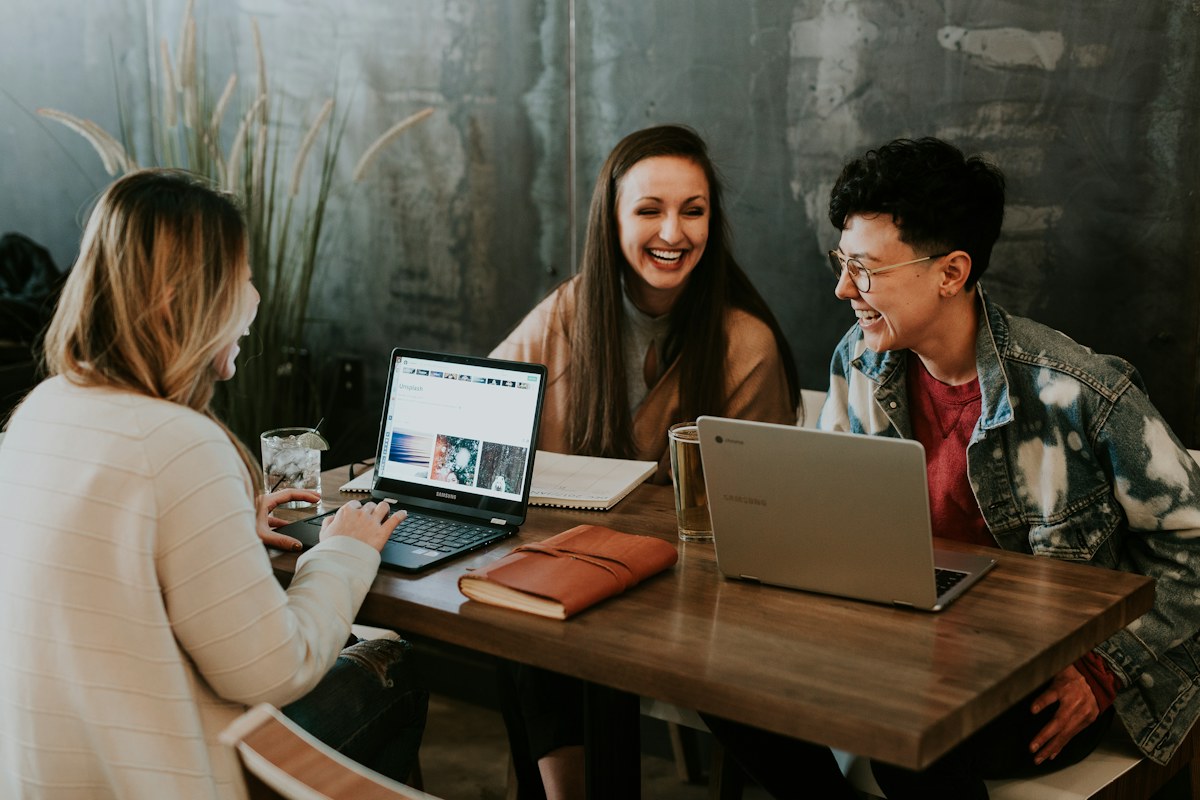 Three colleagues collaborate around a laptop at a shared work table.